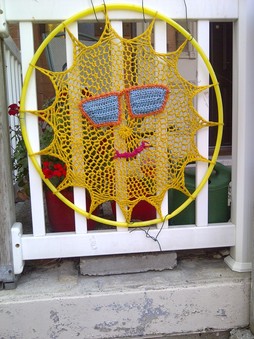 A hula hoop encircles a large crocheted yellow smiling sun wearing sunglasses.